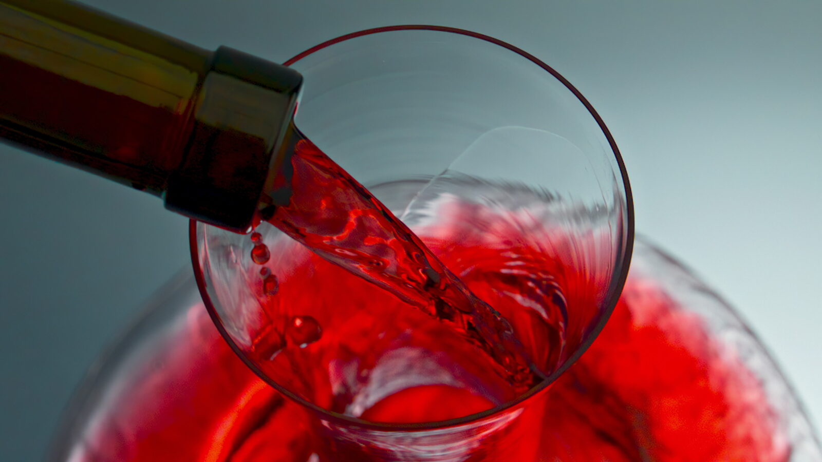 Red wine stream pouring glassware from bottle neck. Rose drink filling decanter